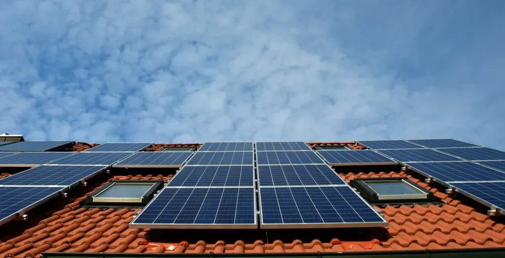Auf einem roten Ziegeldach installierte Sonnenkollektoren unter blauem Himmel mit vereinzelten Wolken – berechnen Sie Ihre Kosten mit unserem Online-Preisrechner für Solaranlagen.